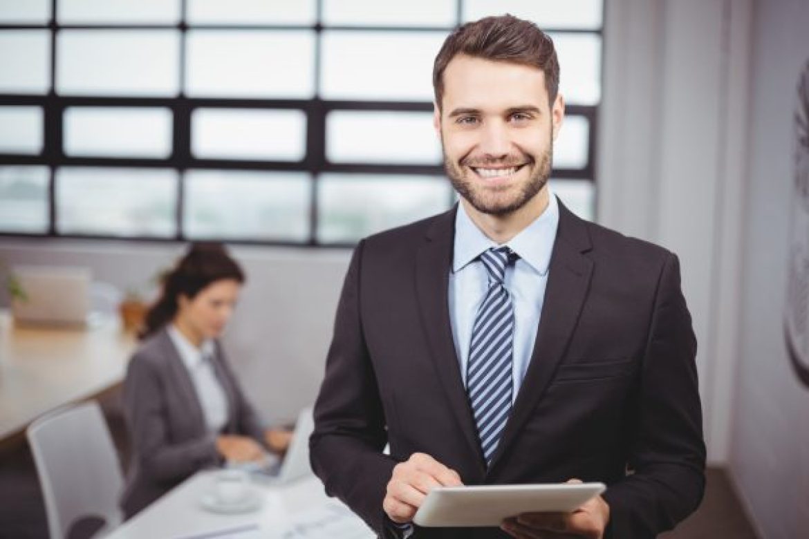 Portrait of confident young businessman using digital tablet while colleague in background